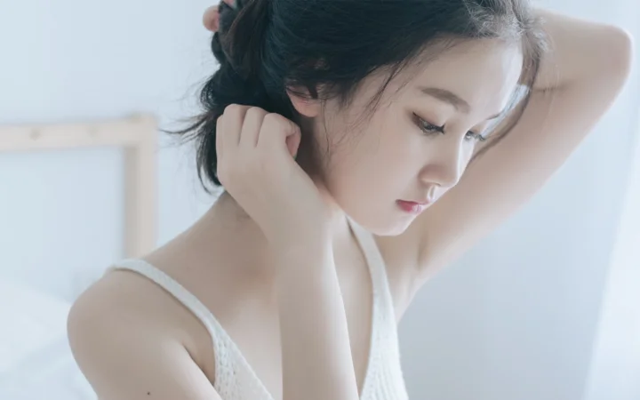 一名黑发女性身穿白色无袖上衣，侧身低头整理头发。