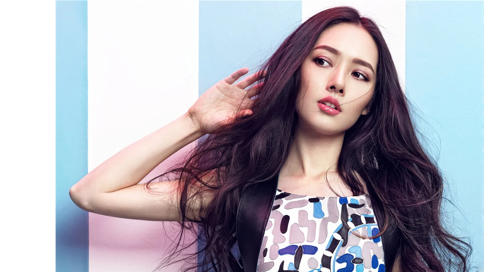 一名长发女性身穿图案上衣，在浅蓝色背景前摆出时尚肖像姿势。