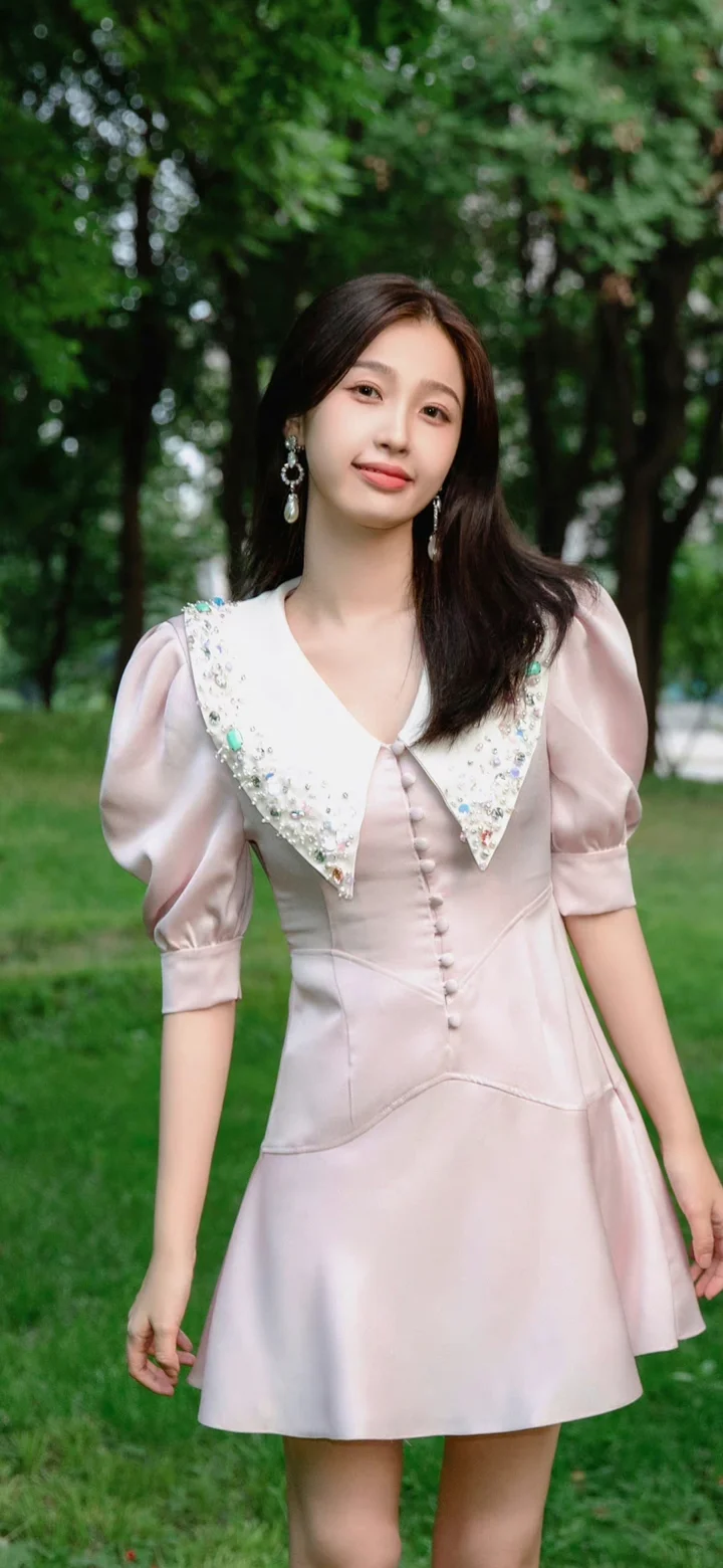 一名成年女子身穿粉色连衣裙站在绿树环绕的户外环境中。