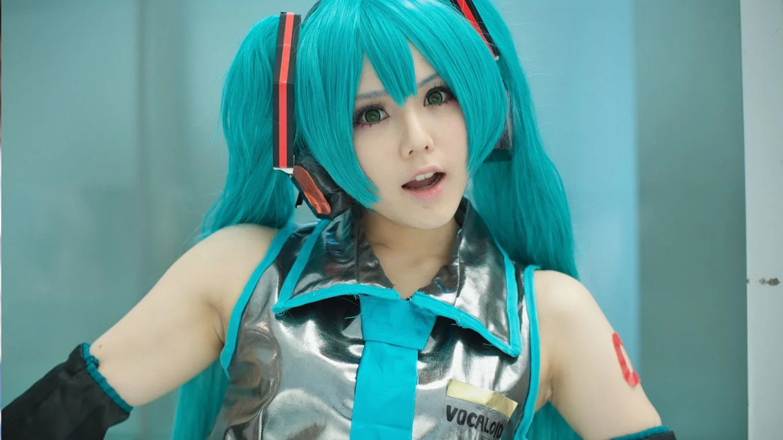 青緑色のツインテールとメタリックな衣装の女性コスプレイヤーがカメラに向かっている。
