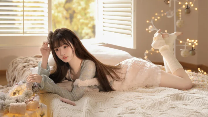一名长发女性趴在温暖明亮的卧室床上。