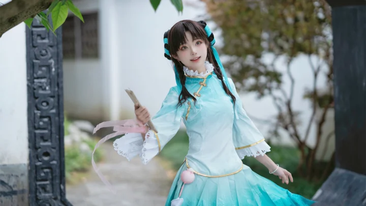 一名身穿浅蓝色传统服饰的女性在庭院树木旁手持折扇摆姿势。