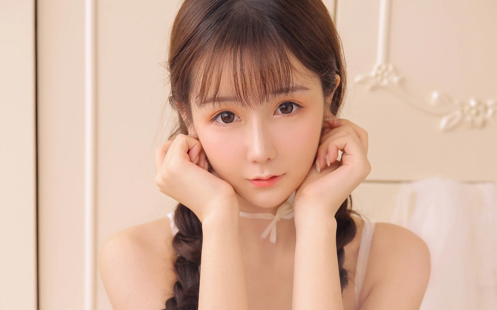 茶色の髪の女性が両手で頬を支え、柔らかな光の中でカメラを見つめています。
