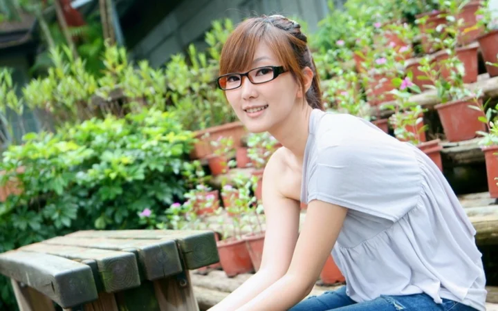 안경을 쓴 여성이 화분 식물로 가득한 정원에 앉아 있습니다.