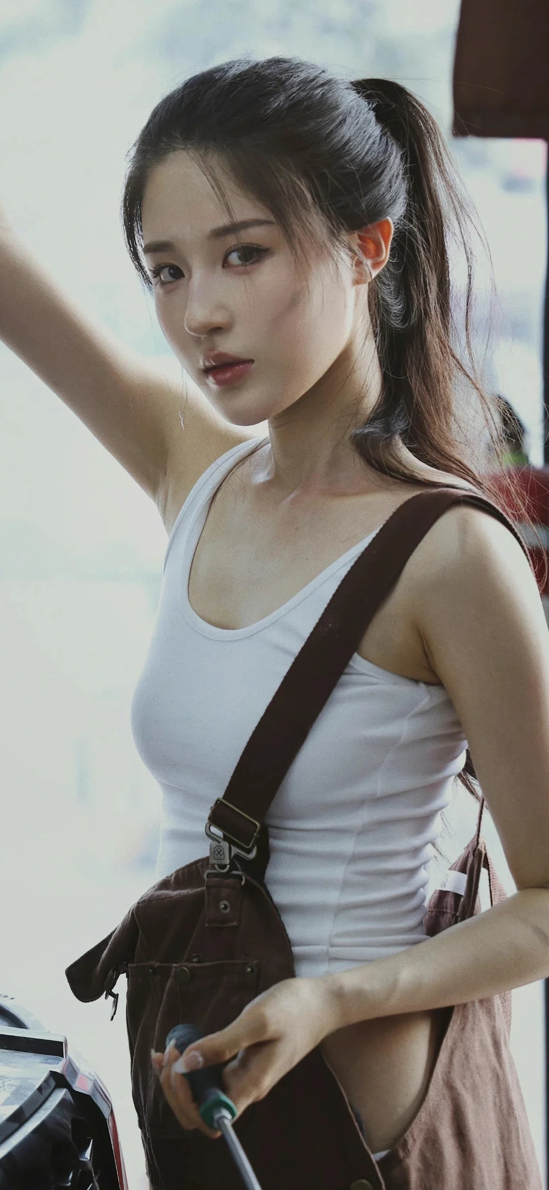 一名扎着马尾、穿白色背心并背着肩包的女子站在画面中央。