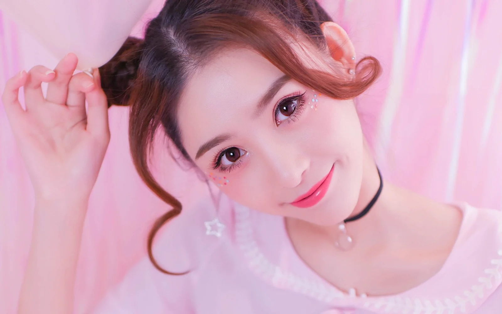 ピンクの背景の前で成人女性が微笑む、柔らかく明るいポートレートです。