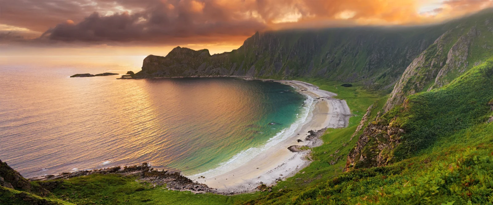 夕阳映照着群山、海湾与弧形沙滩，构成壮丽的海岸风景。