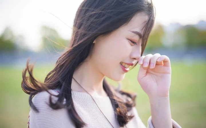一名长发女性在户外阳光下轻抚鼻尖，呈现柔和的侧脸特写。