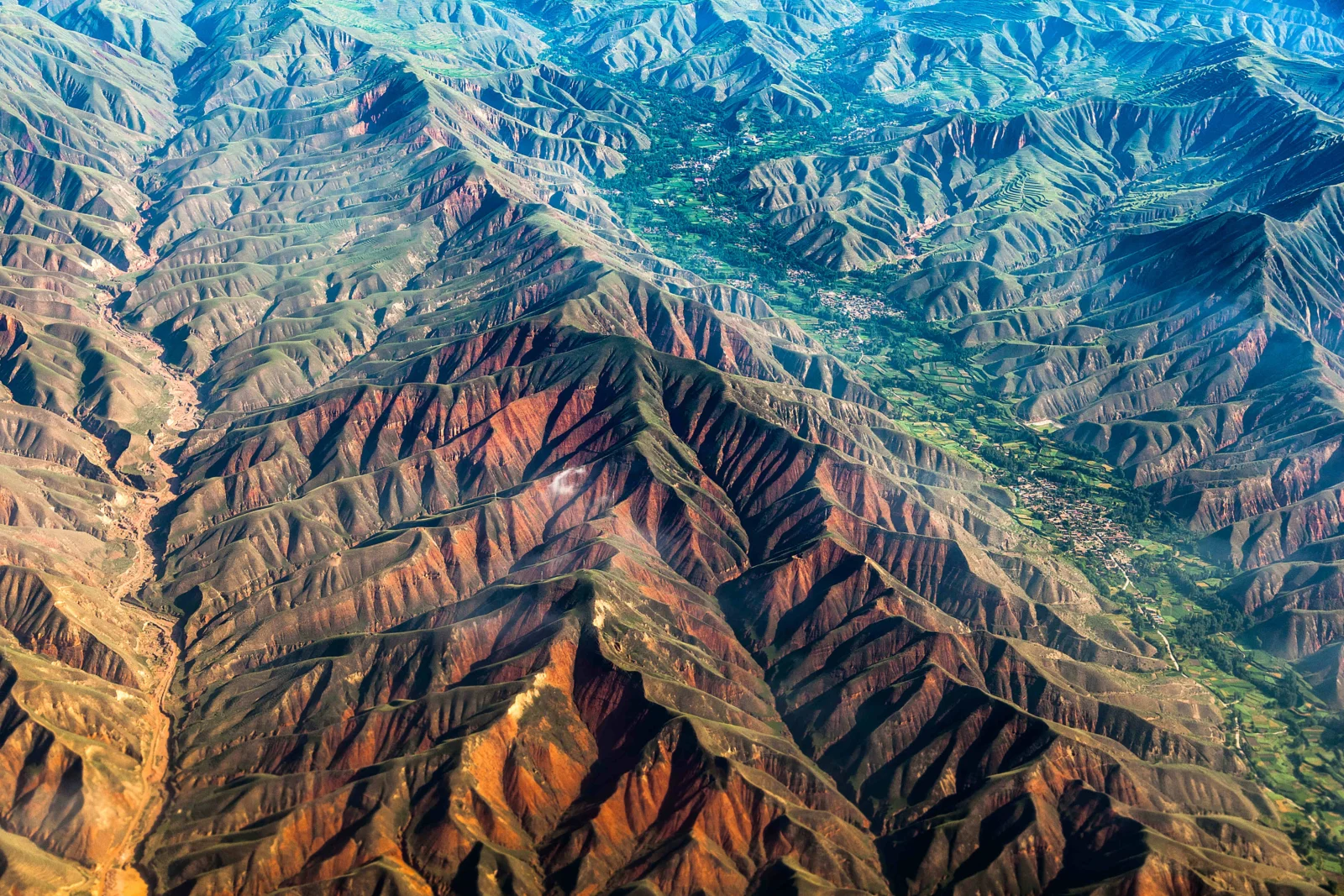 上空から、連なる山々と深い峡谷、山間の緑豊かな谷を見渡している。