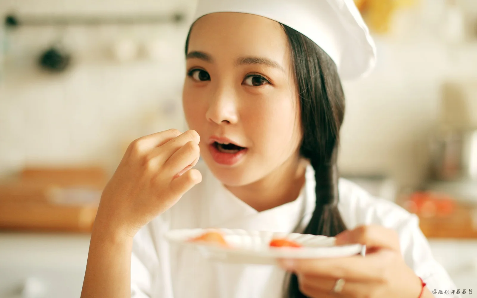 白いコック帽をかぶった女性が皿を持って食事をしている。