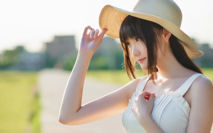 一名成年女性在户外阳光下佩戴草帽并望向一侧。