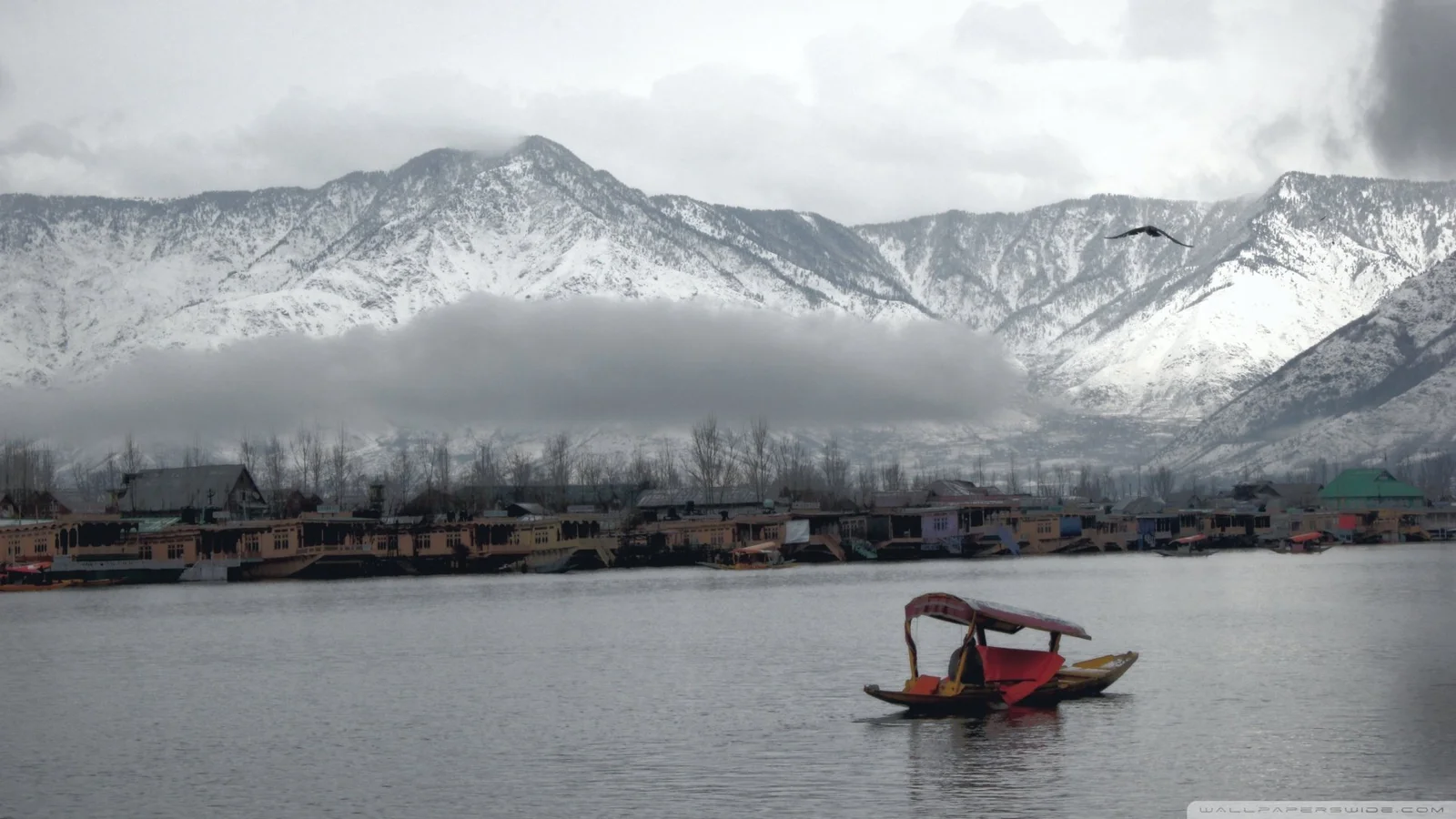 小舟が湖面に浮かび、遠くには雲に包まれた雪山と湖畔の集落が見える。