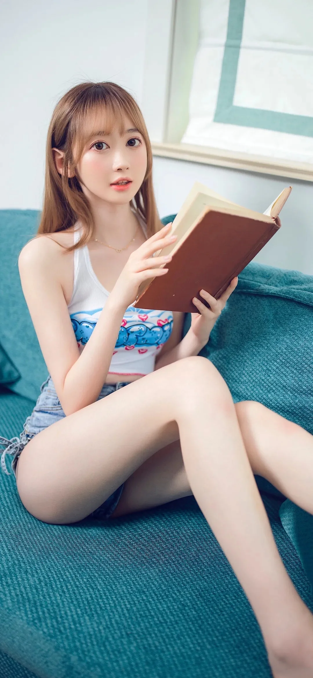 女性が青緑色のソファに座り、開いた本を手にしている。