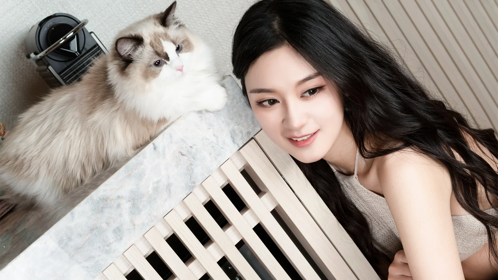 黒髪の女性がピアノのそばに寄り添い、隣にはふわふわの猫がいます。