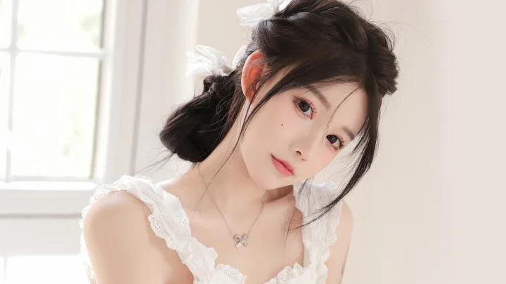 一位成年女性穿着白色蕾丝上衣，在明亮窗边侧头面对镜头。