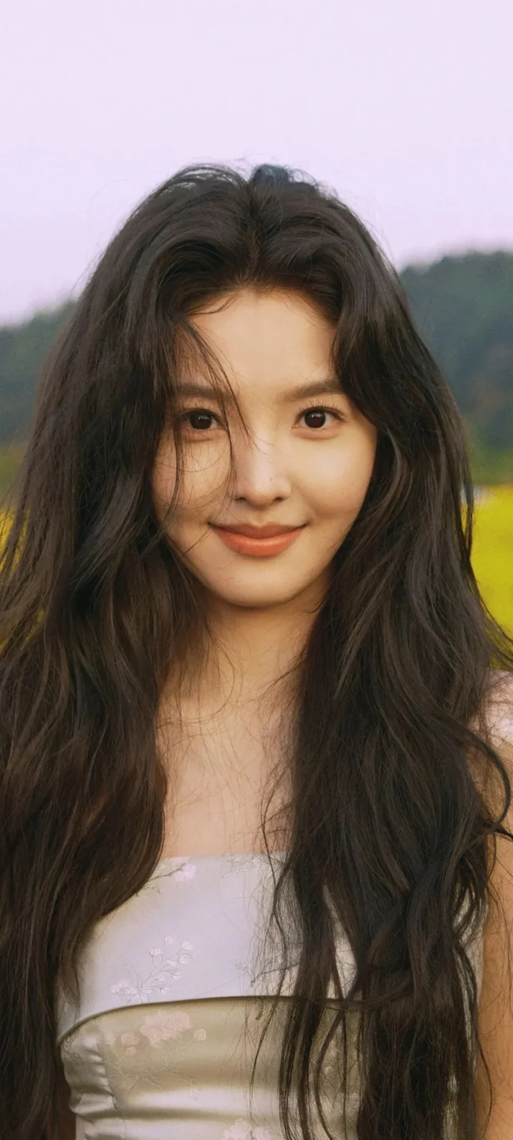 一名长发女性在户外背景前面向镜头微笑。