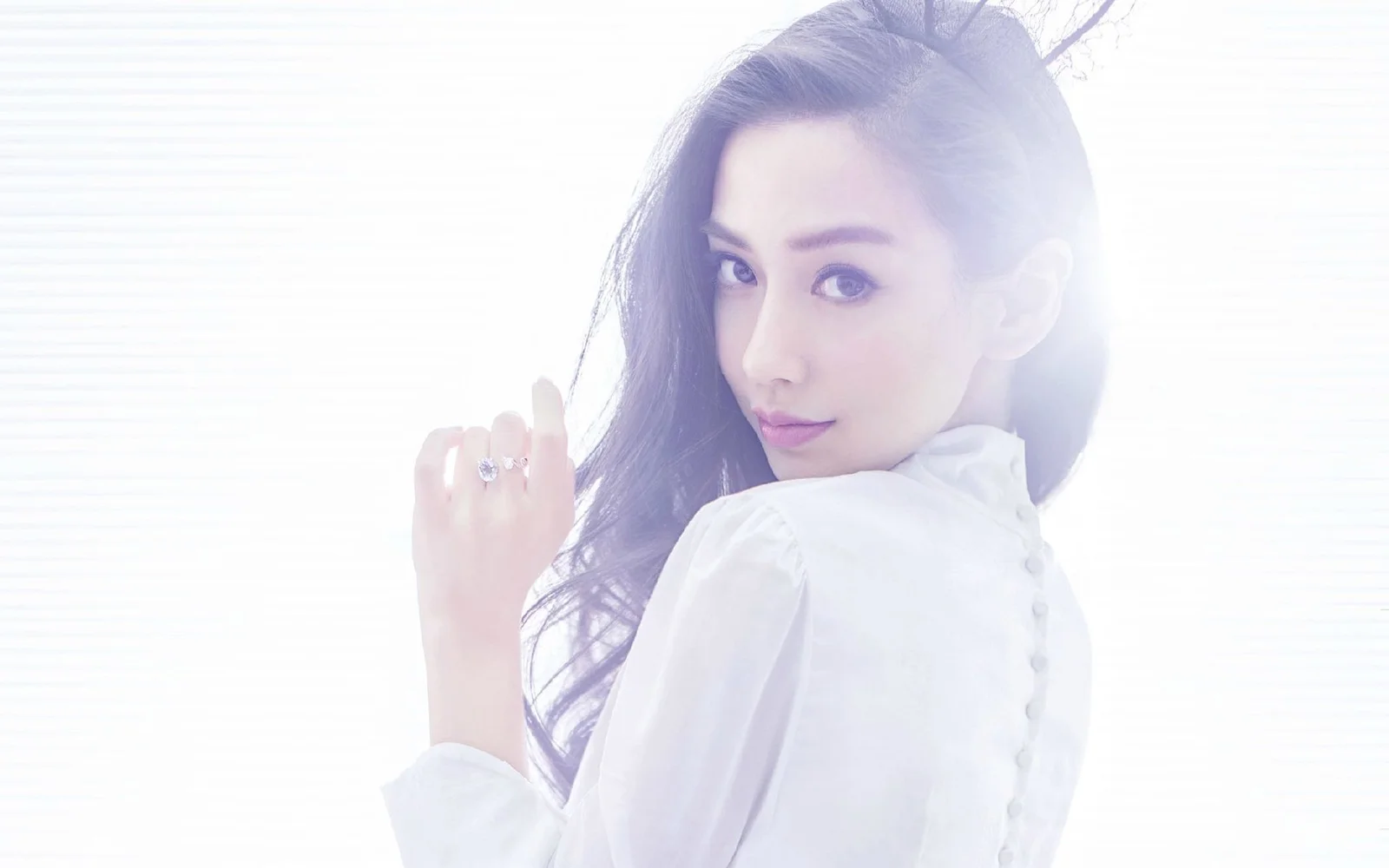 一位长发女性穿着白色上衣回头看向镜头，画面以柔和明亮的白色调为主。