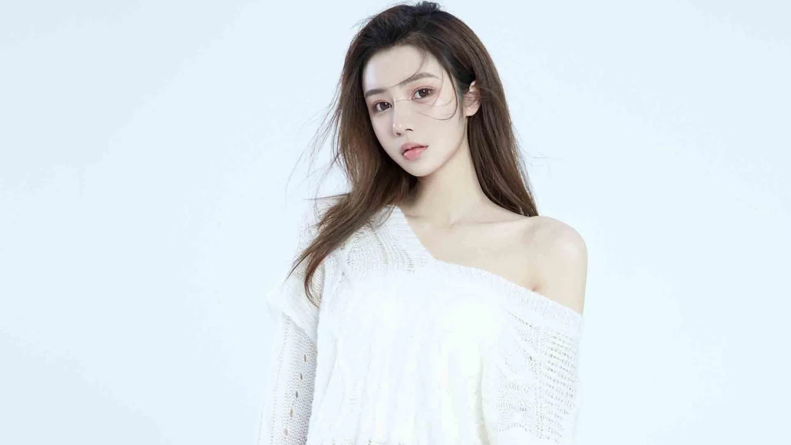 一位成年女性身穿白色针织衫，站在浅蓝色背景前。