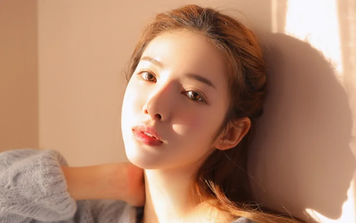 一位女性靠在墙边，脸庞沐浴在温暖的阳光中。
