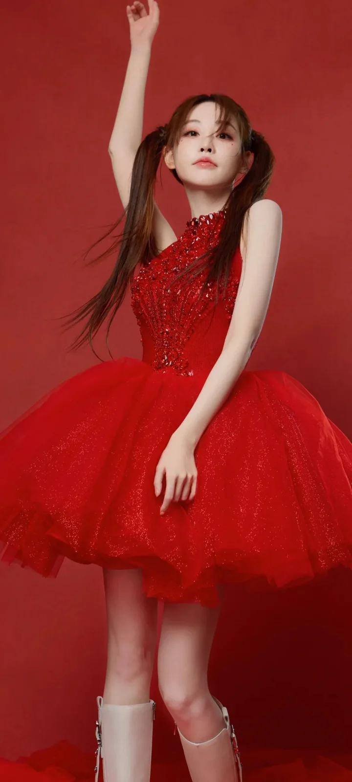 一名身穿紅色亮片禮服的女子站在紅色背景前，一隻手臂向上伸展。