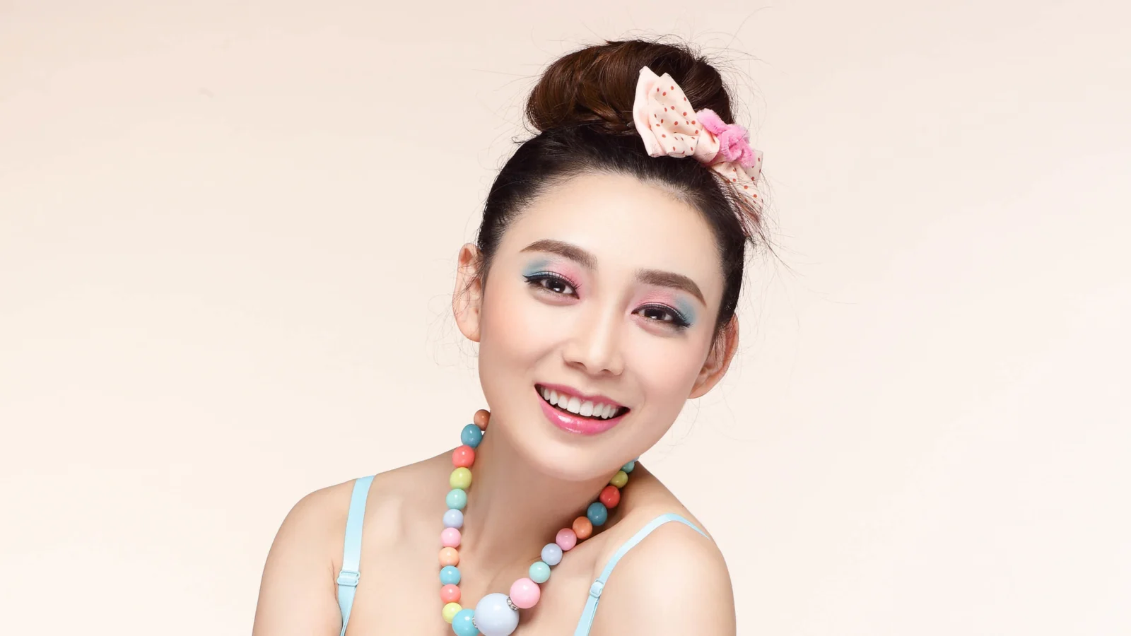 밝은 배경 앞에서 화려한 목걸이와 헤어 액세서리를 착용한 웃는 여성이 인물 사진을 촬영하고 있습니다.