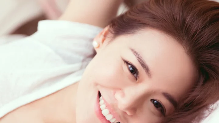 성인 여성이 누워 미소 짓고 있으며 얼굴이 화면 대부분을 차지합니다.