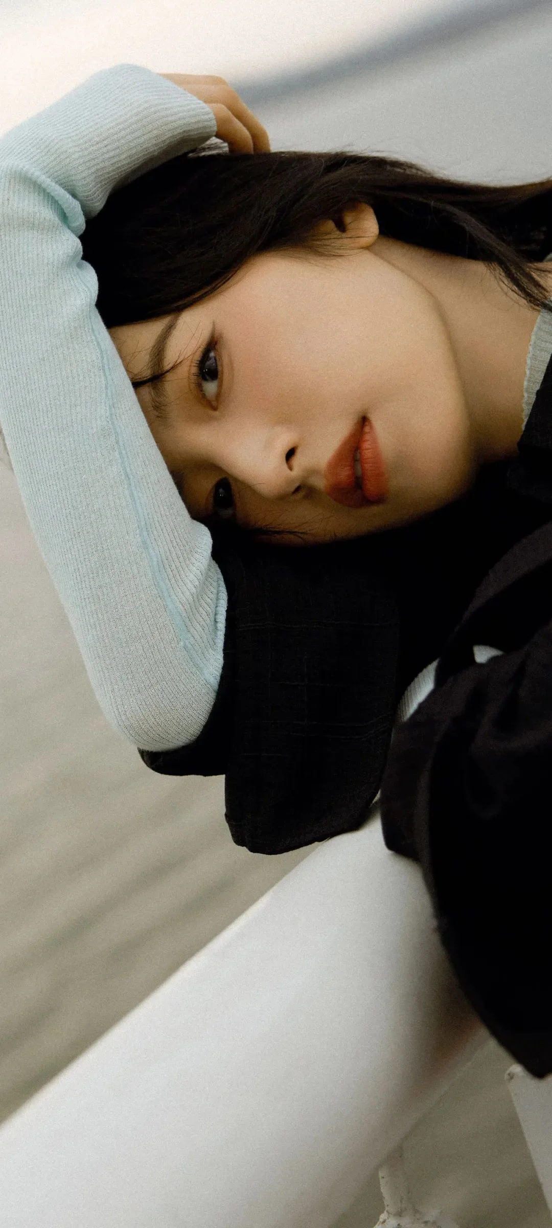 검은 머리의 여성이 밝은 배경 위에 옆으로 누워 한쪽 팔을 머리 가까이에 둔 얼굴 클로즈업이다.