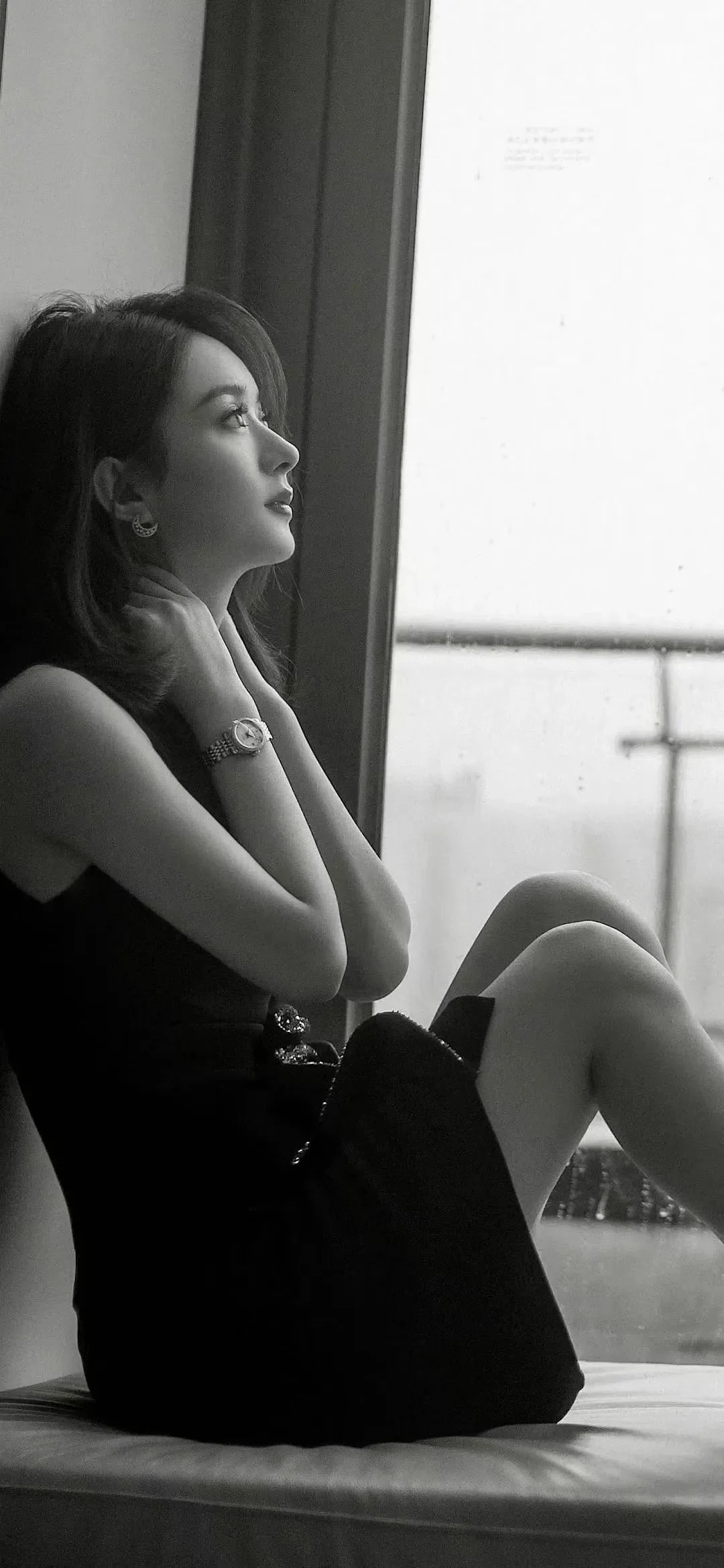 一位身穿黑色无袖连衣裙的成年女性坐在窗边，画面为黑白色调。
