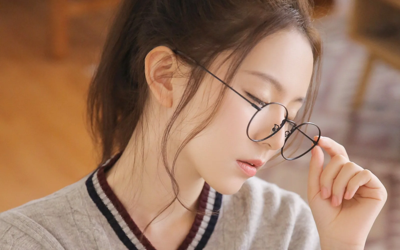 둥근 안경을 쓴 여성이 안경테를 살짝 만지는 모습을 따뜻한 색감의 배경과 함께 가까이 담았습니다.