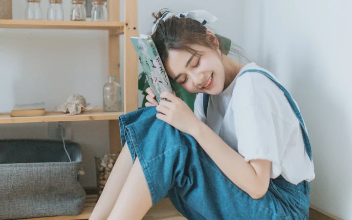 一位成年女性在室内靠着书本微笑休息，背景是木架与家居陈设。