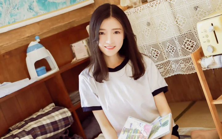 一名长发女子坐在室内，面带微笑并手持一本打开的书。