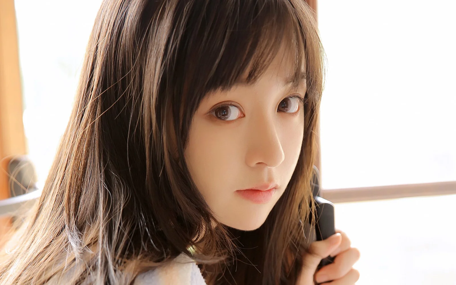 室内の窓辺にいる茶髪の女性のクローズアップポートレート。