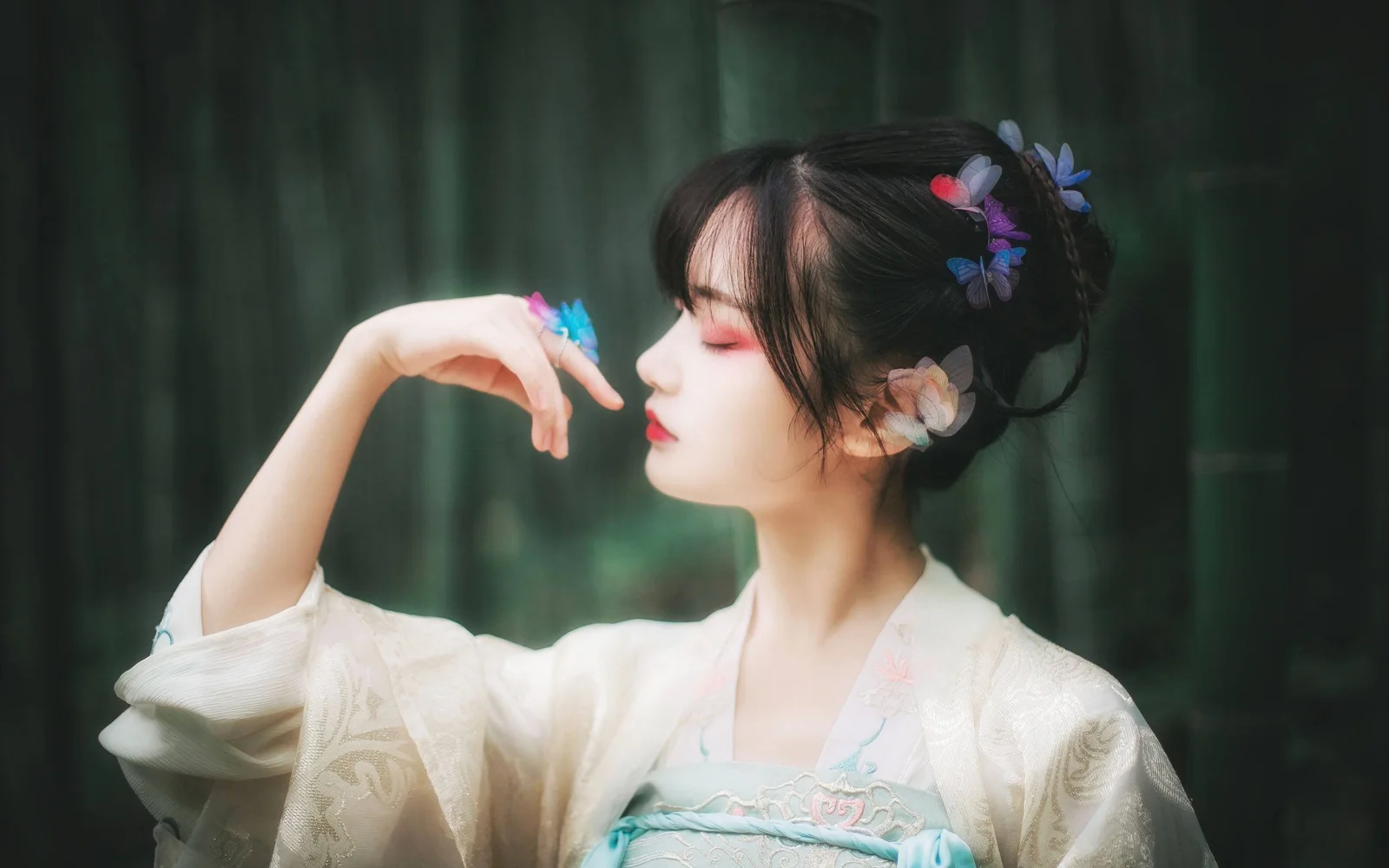 一位身穿浅色传统风格服饰、佩戴花朵发饰的女子在深绿色树林背景前侧脸抬手。