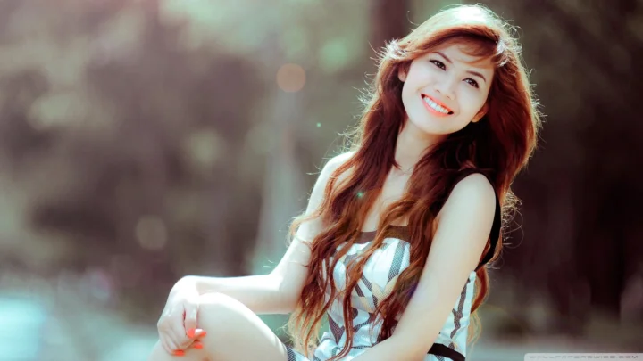 一名长发女性在户外背景前微笑坐姿的横向肖像照片。