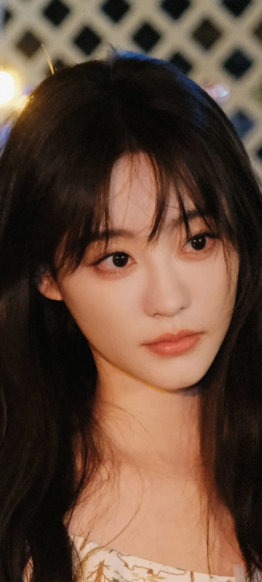 黒髪の女性を写した近接ポートレートで、背景にはぼやけた幾何学模様が見えます。