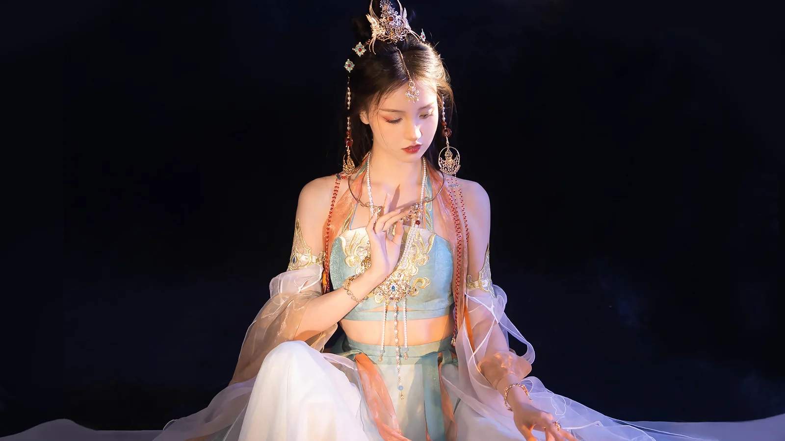 一名身着华丽传统服饰并佩戴精致头饰的女子坐在深色背景前。
