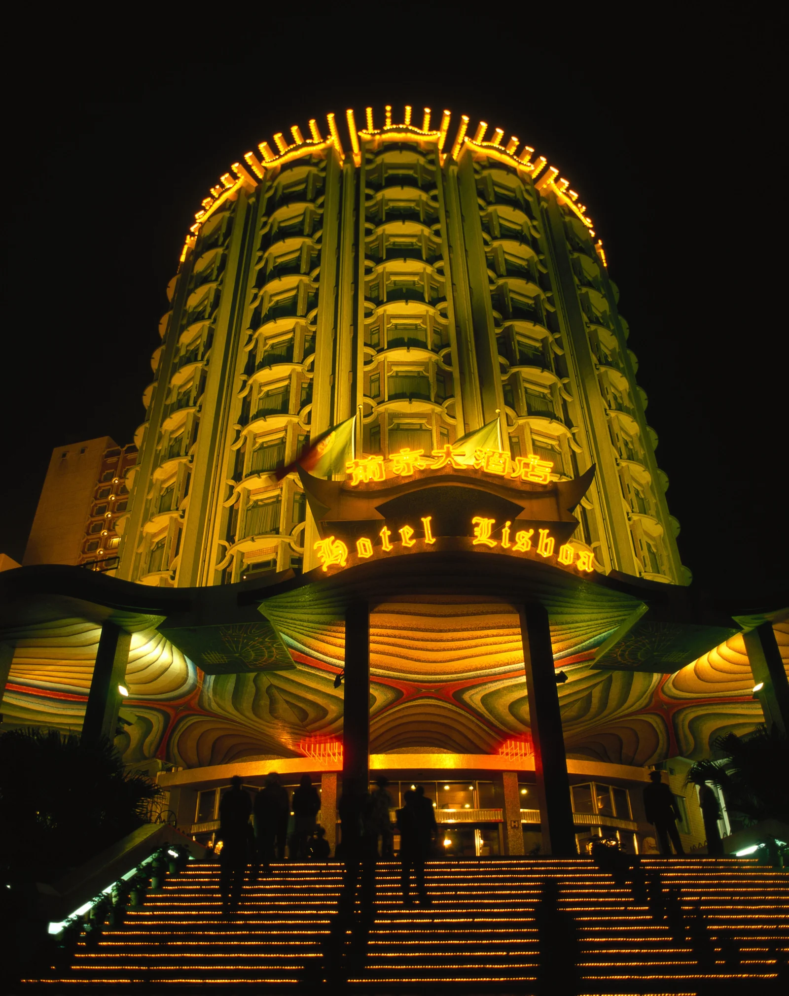 夜色中的高层酒店被金色灯光照亮，入口台阶延伸至画面前景。