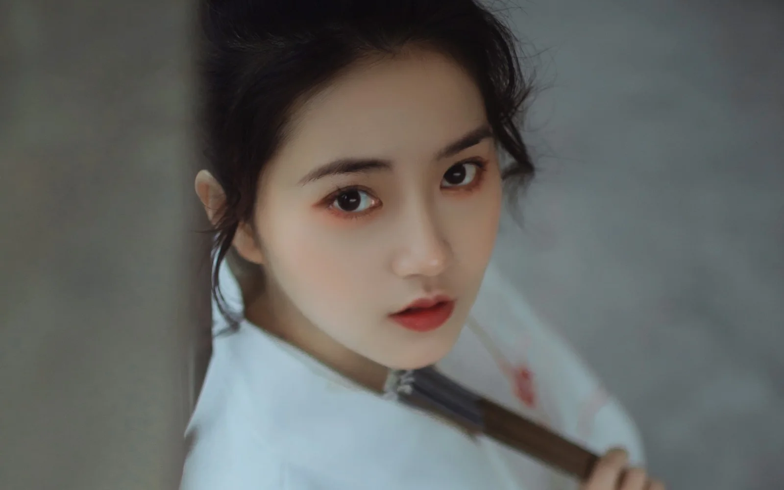 부드러운 회색 배경을 뒤로하고 여성이 카메라를 바라보는 클로즈업 인물 사진입니다.