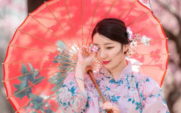 꽃무늬 기모노를 입은 여성이 붉은 일본식 우산 앞에서 포즈를 취하고 있다.