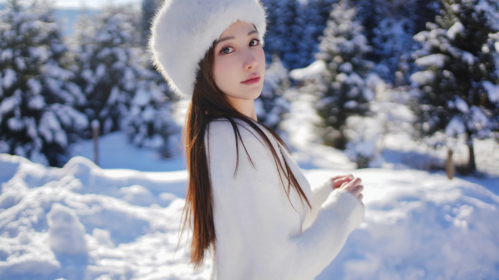 白いファーハットをかぶった成人女性が雪に覆われた森の中に立っています。