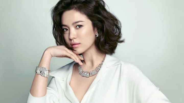 밝은 배경 앞에서 흰 셔츠를 입은 성인 여성이 우아한 포즈를 취하고 있습니다.