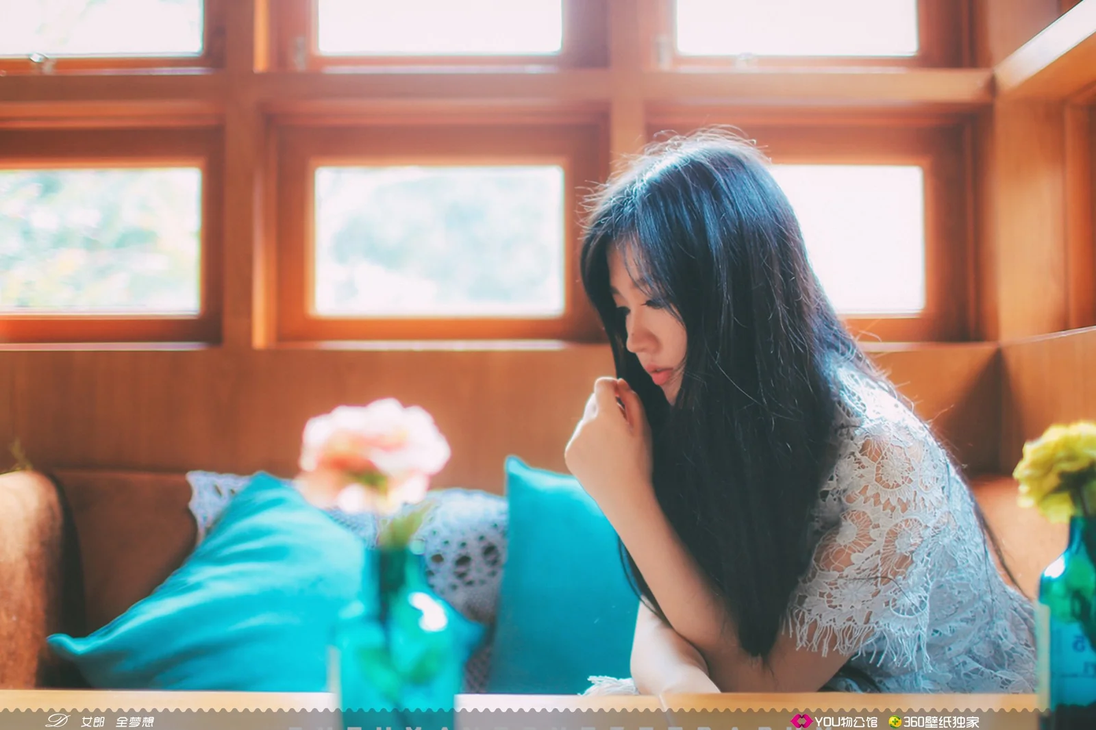 한 여성이 나무 창문 옆 소파에 앉아 따뜻한 햇빛이 실내로 들어오고 있다.