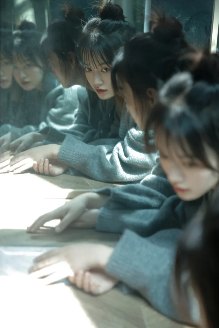 一名穿灰色针织衫的女子靠在桌边，镜面映出她的多个倒影。