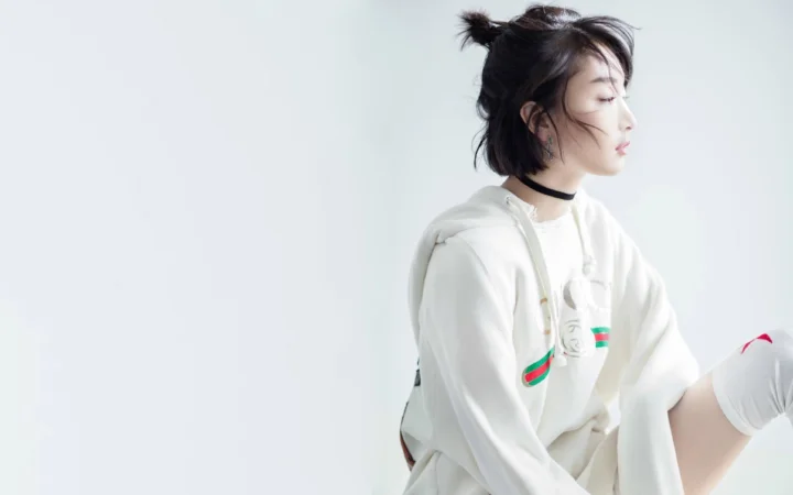 一名穿白色上衣的女性侧身坐在浅灰色背景前，面向右侧。
