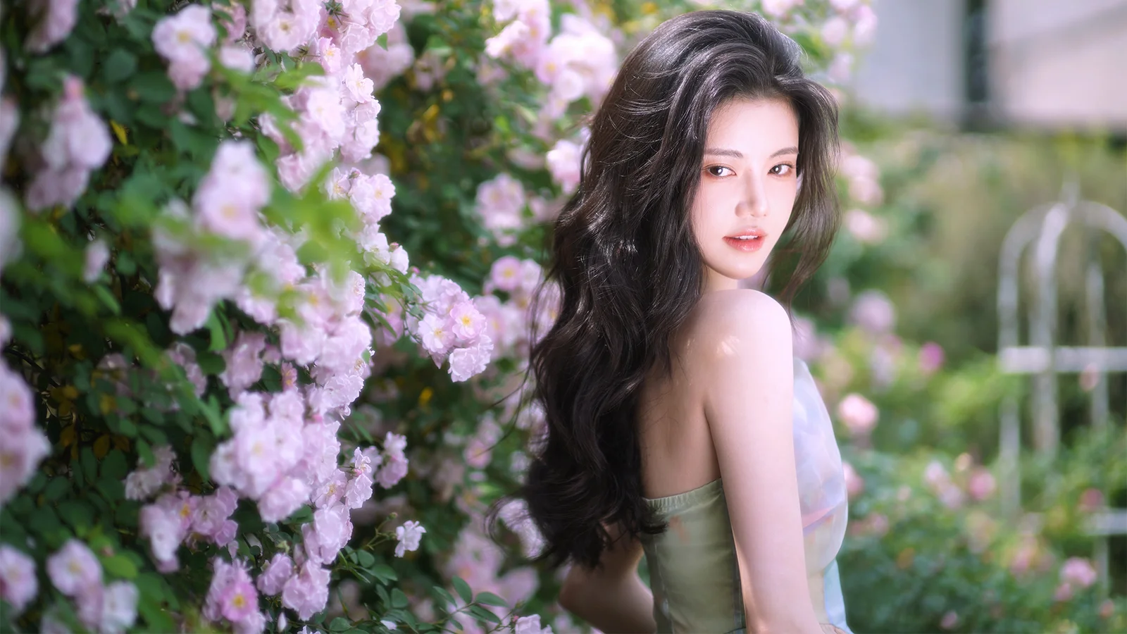 一名女子站在盛开粉色花朵的花园中回望镜头。