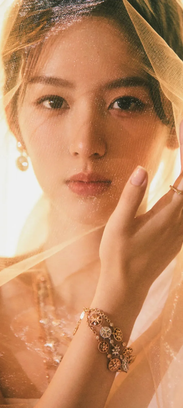 一名成年女性被金色薄紗和珠寶映襯著，面部佔據畫面主體。