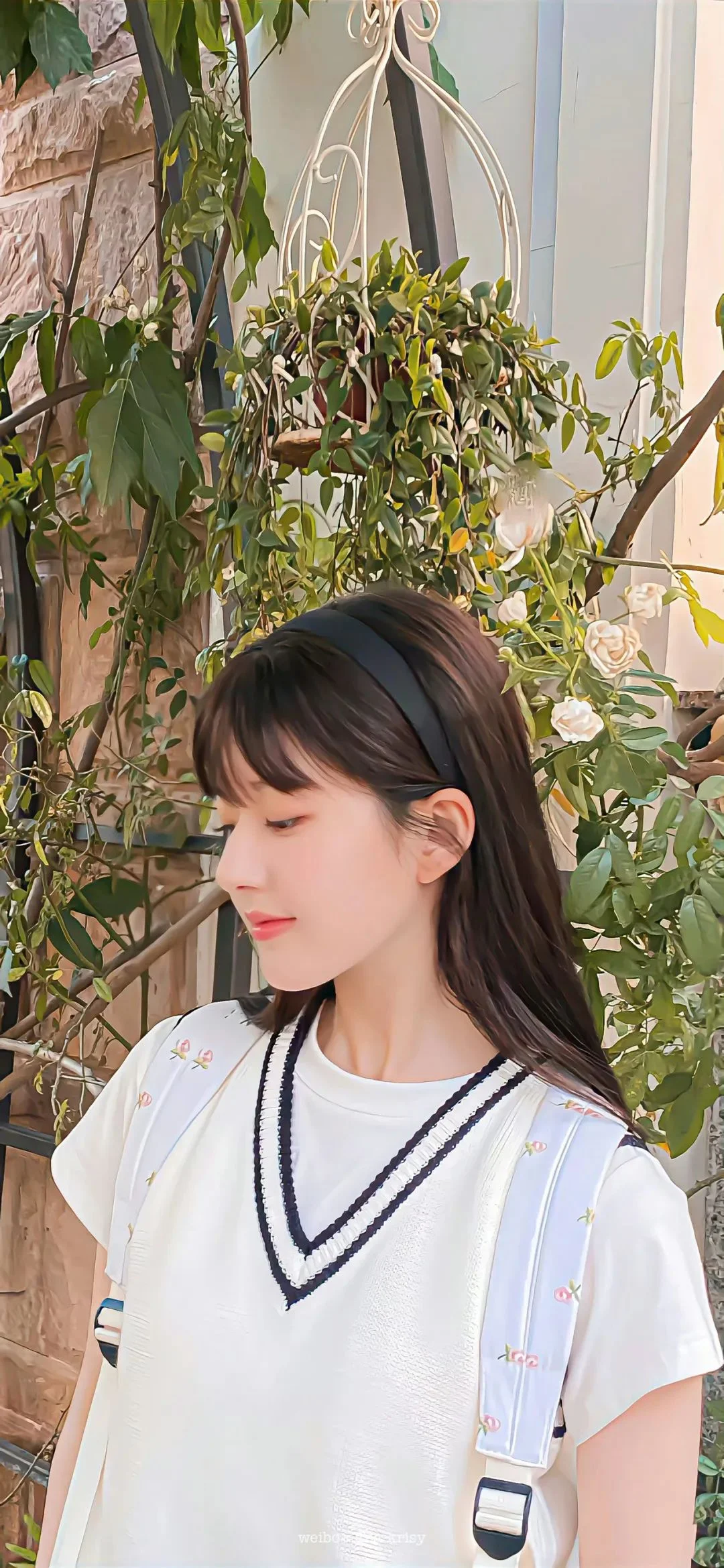 一位身穿白色上衣的女性站在绿植旁，侧头低头望向一侧。