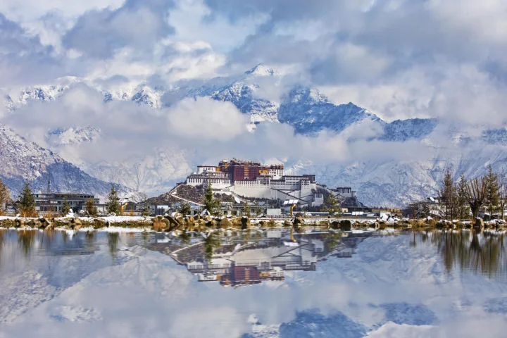 湖面倒映着雪山环绕的宫殿建筑，天空中云层交织。