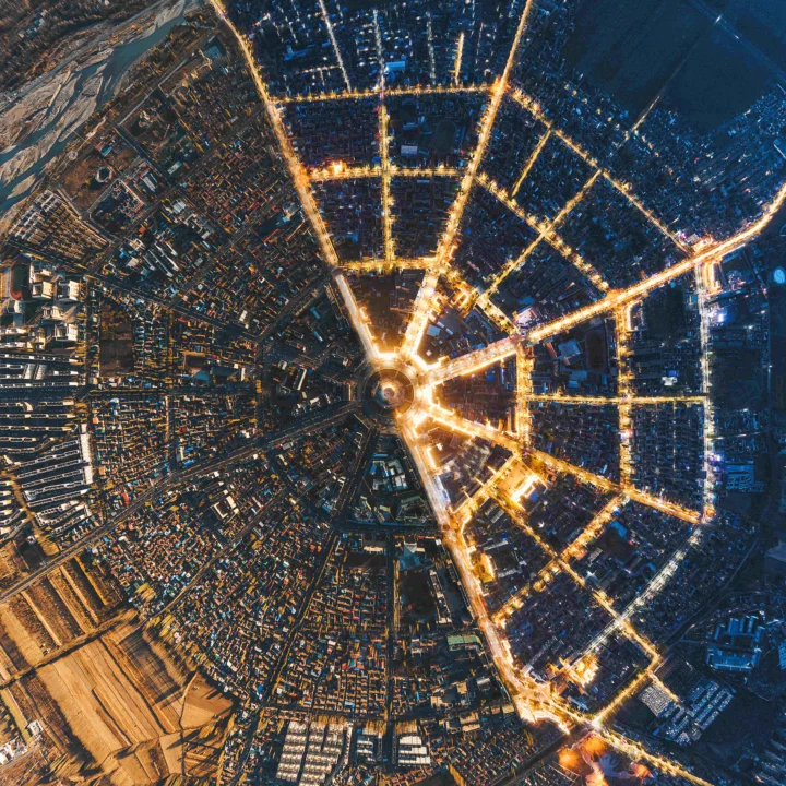 俯瞰夜晚城市，明亮街道从中心向四周延伸成放射状网络。