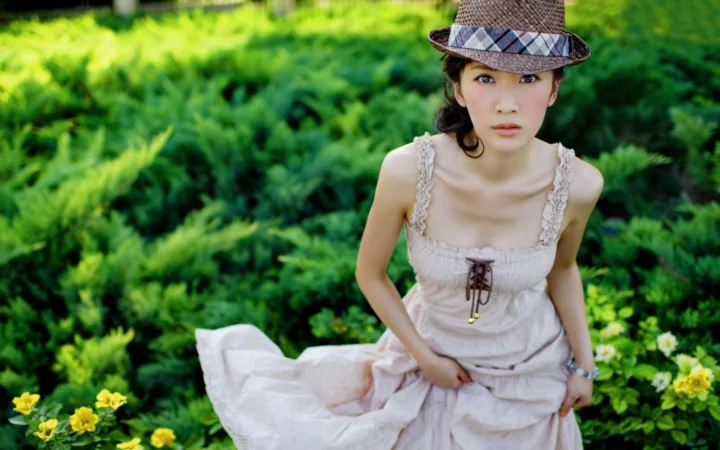 一名戴着帽子、穿着浅色连衣裙的女子坐在绿意盎然的花园中。